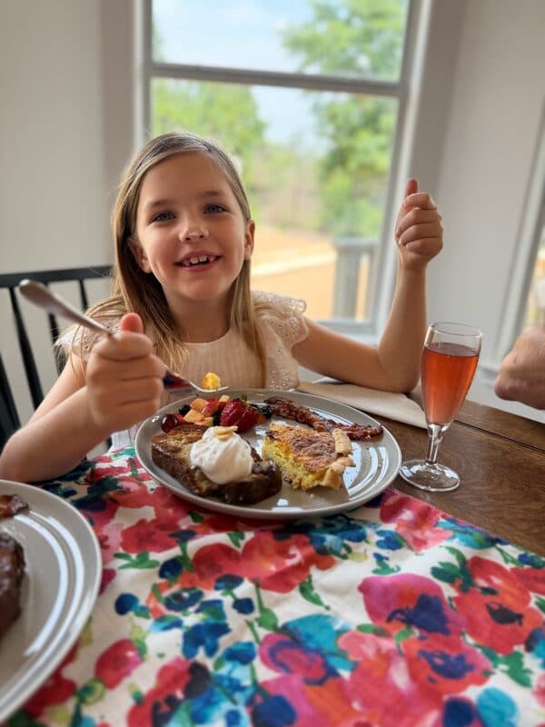 A young girl giving a thumbs-up next to her plate of Mother's Day Brunch Kit French Toast and quiche