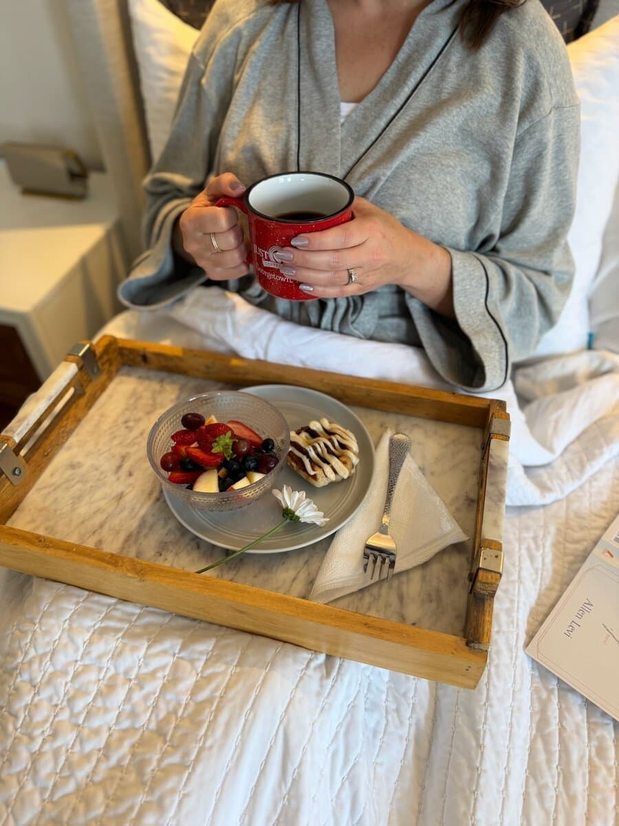 A mom in her robe holding the red Just Love Georgetown ceramic mug with a breakfast tray on her lap