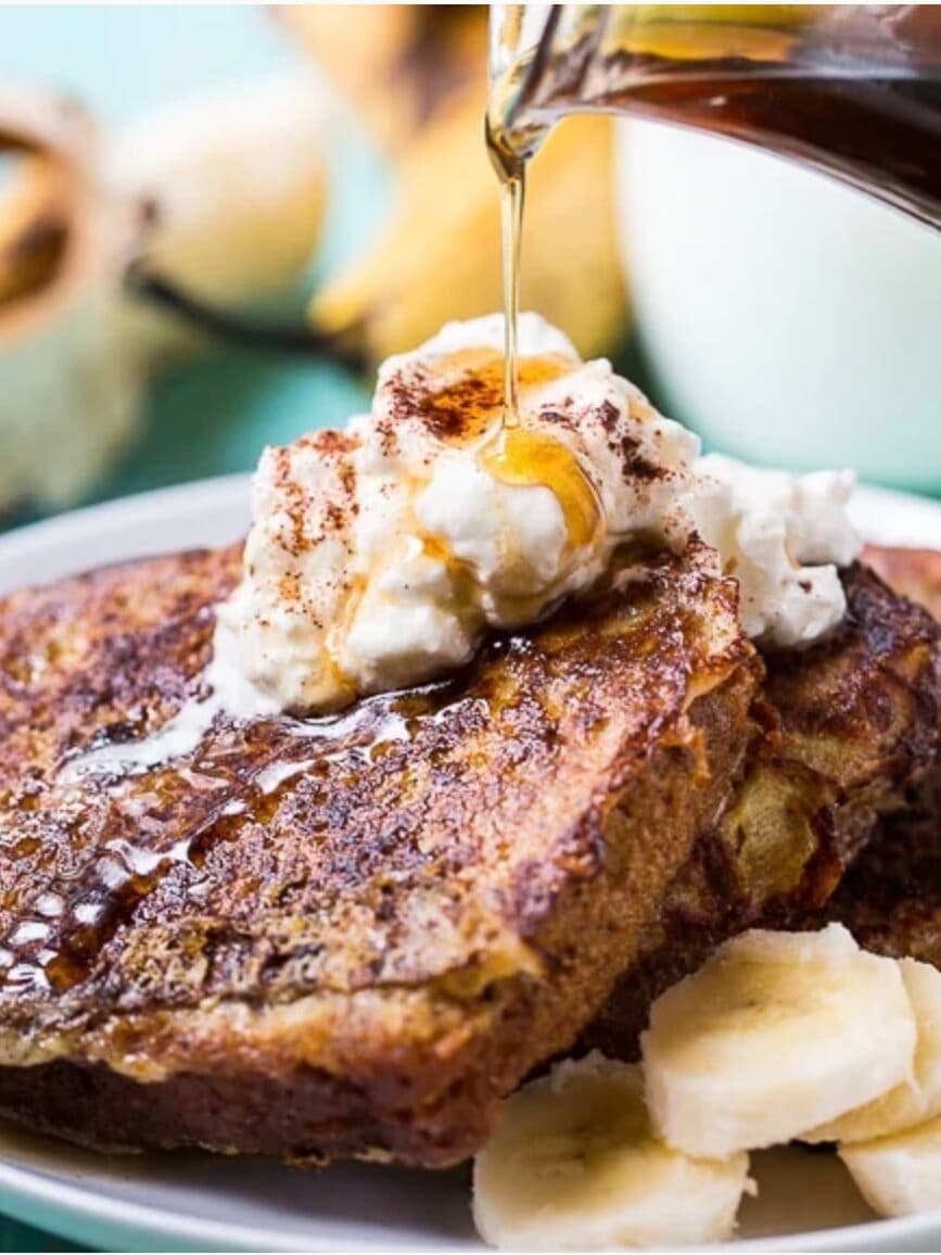 Chef's Banana Bread French Toast with whipped cream, banana slices, and maple syrup on a plate