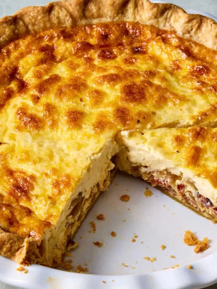 A whole golden Just Love Quiche in a pie dish with one slice cut out